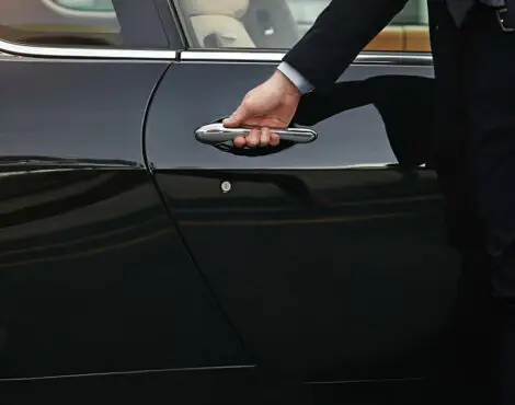 A person in business attire opens the door of a black car, suggesting the discreet service of a professional chauffeur Southampton offers, with only their arm and torso visible.