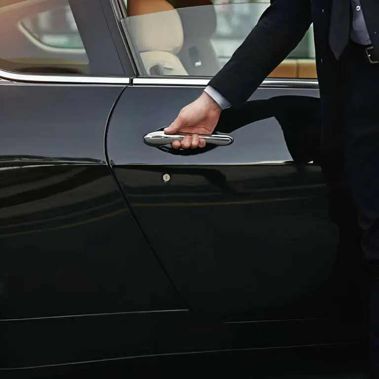 A person in business attire opens the door of a black car, suggesting the discreet service of a professional chauffeur Southampton offers, with only their arm and torso visible.