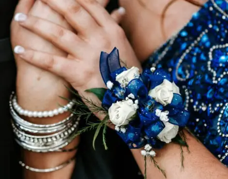 Close-up of a person wearing a blue and white corsage, hands resting on another’s arm—both in formal attire and jewellery, ready to be driven by a chauffeur in Hampshire.