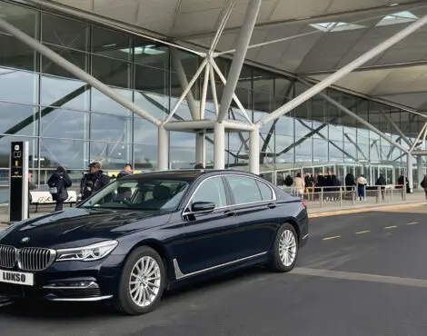 A black BMW saloon with the number plate LUKSO is parked outside Gatwick Airport’s modern terminal, featuring glass windows and a covered entrance.