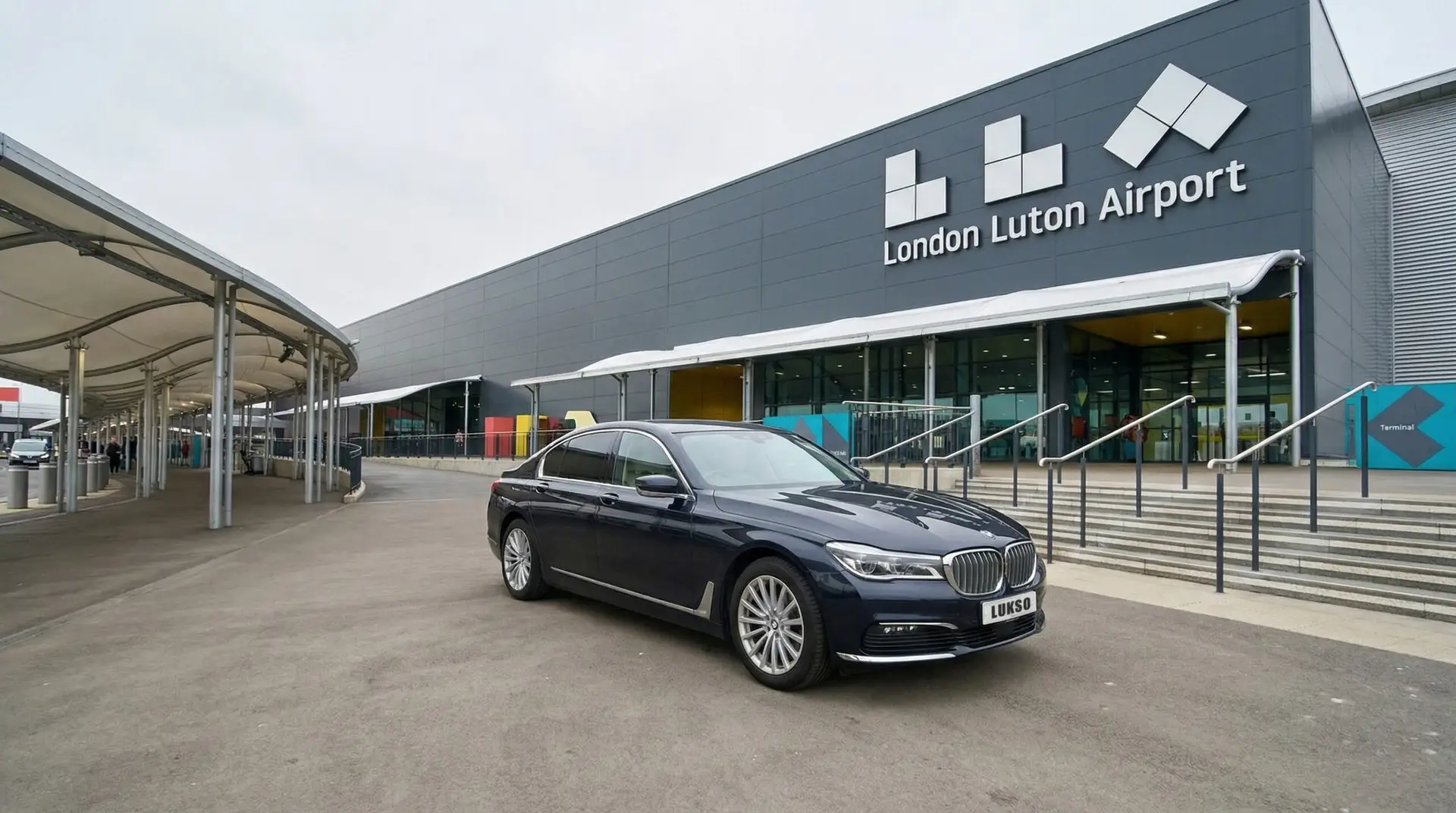 A black BMW saloon parked outside the entrance of Luton Airport, with the airport building and sign visible in the background.