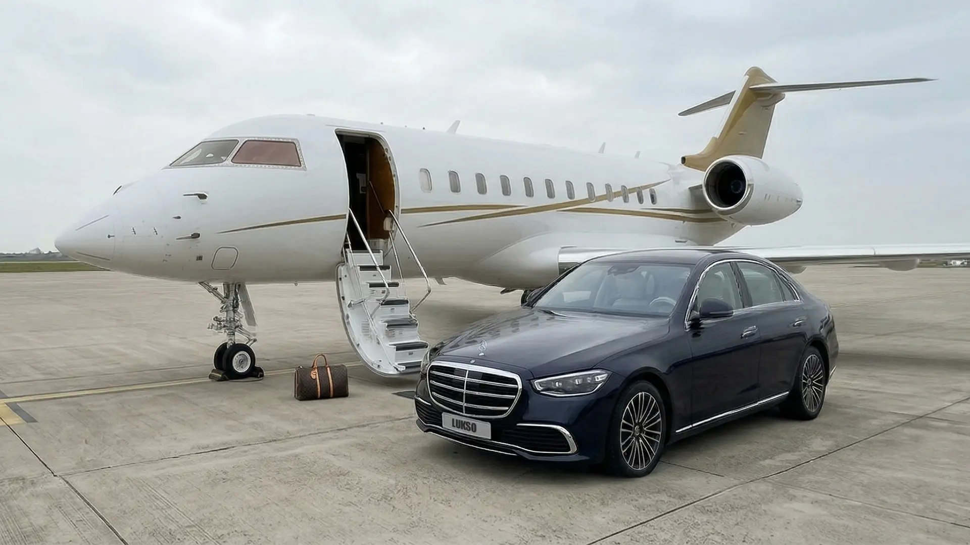 About Lukso Travel: A private jet is parked on an airport apron with its door open and a set of stairs down. Nearby, a black luxury saloon and a brown travel bag capture the elegance of the Lukso Travel experience.